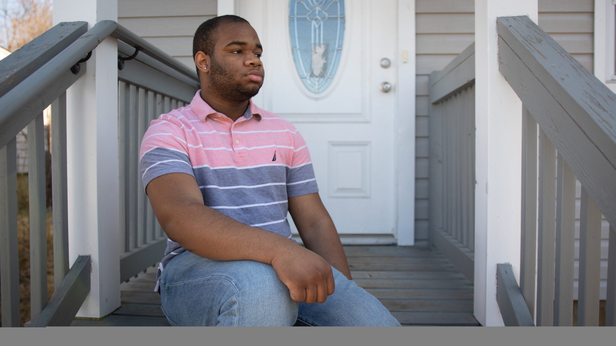 Dark skinned man sits on the steps of a house, staring into the distance